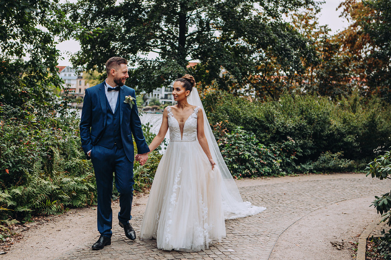 Das Brautpaar halten die Hände und laufen im Park Schloss Köpenick